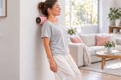 Femme qui masse sa nuque et ses épaules avec le rouleau TriggeRoll calé contre un mur